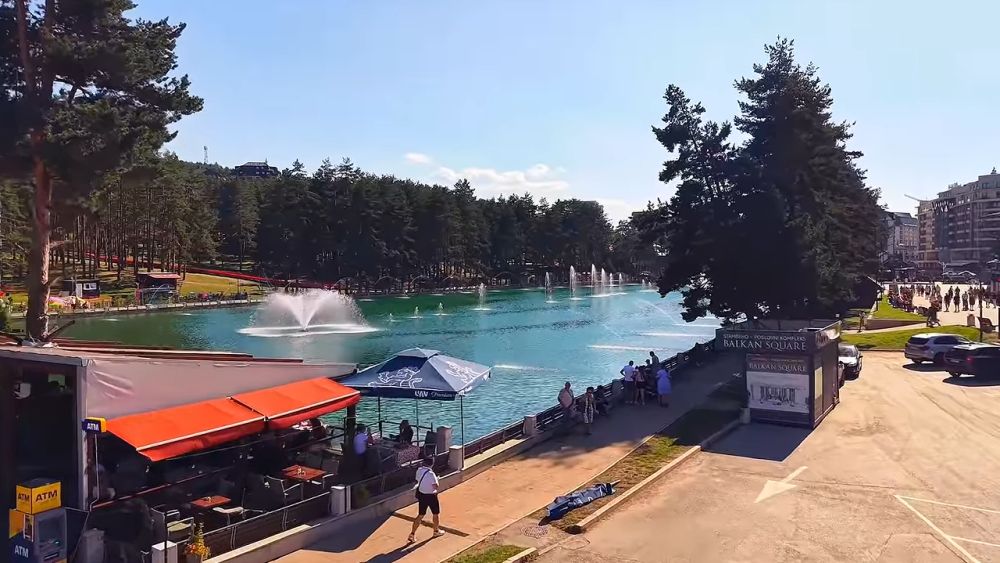 Jezero i savremene zgrade u centru Zlatibora, okruženi borovima i šetalištem.